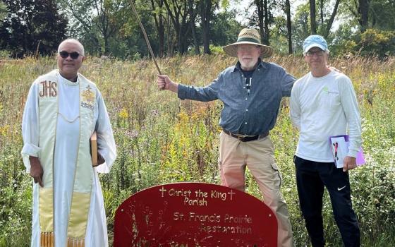 Priest stands in field with two other men.
