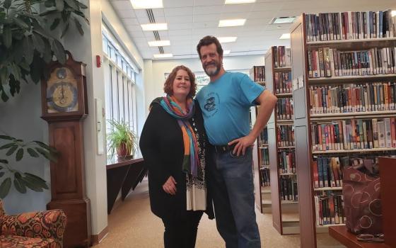Man and woman stand near bookshelves inside library. 