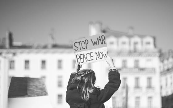 View from the back of a person holding a sign that says: "Stop war. peace now."