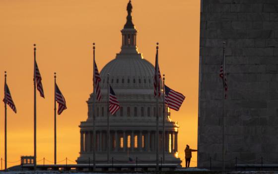 The sky is orange behind the U.S. Capitol dome with American flags flying around it
