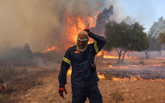 A firefighter walks next to rising flames as a wildfire burns near the village of Vati, on the island of Rhodes, Greece, July 25, 2023. (OSV News/Reuters/Nicolas Economou)