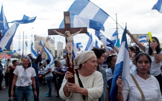 A woman carries a crucifix surrounded by a crowd of other people, many carrying Nicaraguan flags
