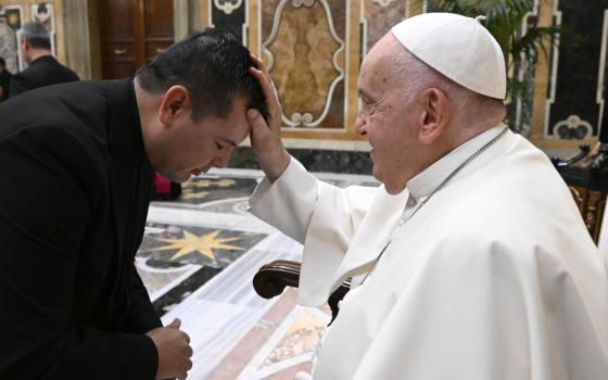 Pope Francis places his hand on the head of a black-haired priests who bows before him