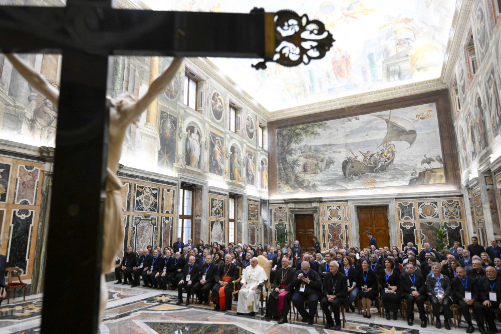 A group photo with Pope Francis in the middle is visible from behind a crucifix