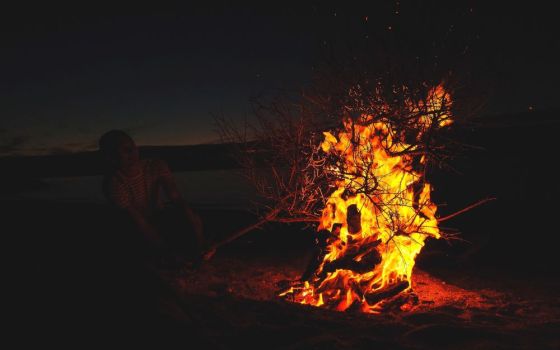 A person near a bonfire on a beach before sunrise in Courtown, Ireland (Unsplash/Traolách Conboy)
