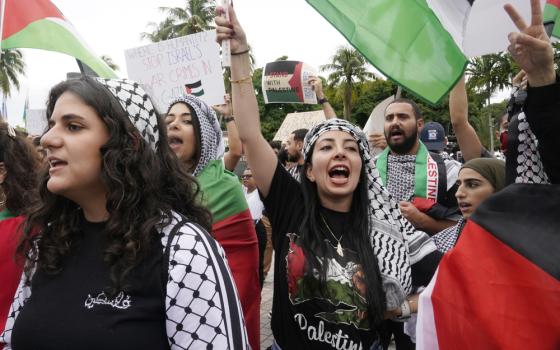 A group of brown people wearing keffiyehs and carrying Palestinian flags shout